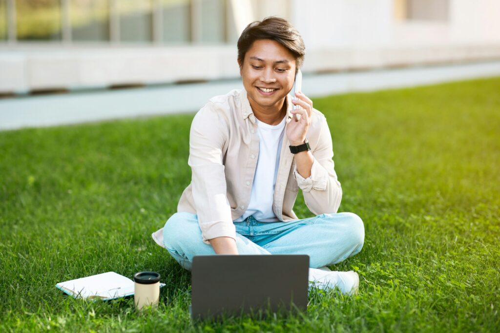 Positive young filipino man manager with laptop calls by phone