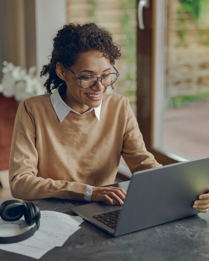 Smiling female manager working remotely on laptop from home while sitting at living room
