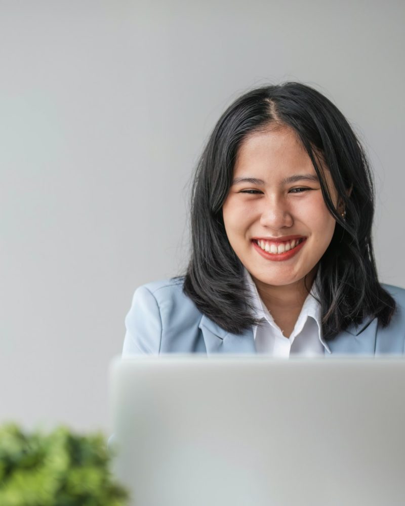 Young smiling Asian business woman employee working on laptop in corporate office. Happy